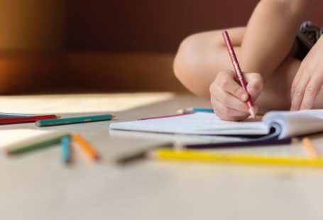 Cognitive Skills - Crop kid sitting on floor and writing in notebook