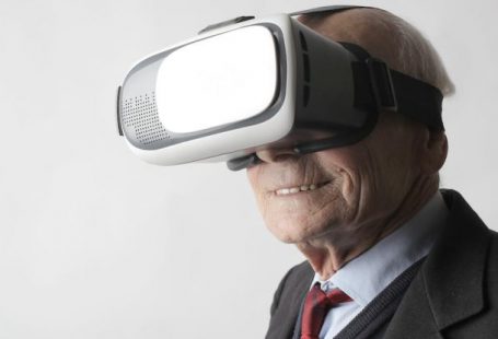 Wearables - Smiling elderly gentleman wearing classy suit experiencing virtual reality while using modern headset on white background